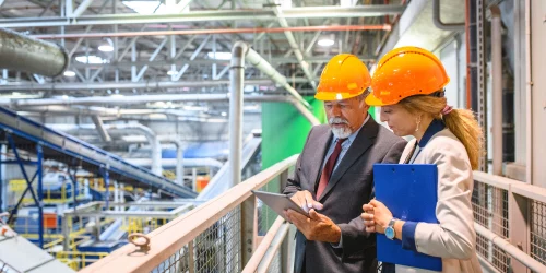 a man and women in safety hats in a factory following ISO 9001 management system