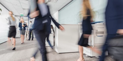 people walking fast through an office corridor